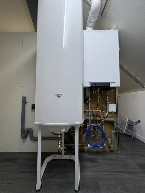 Nordic warmwateraccu op een standaard in een berging, netjes aangesloten op de cv-ketel